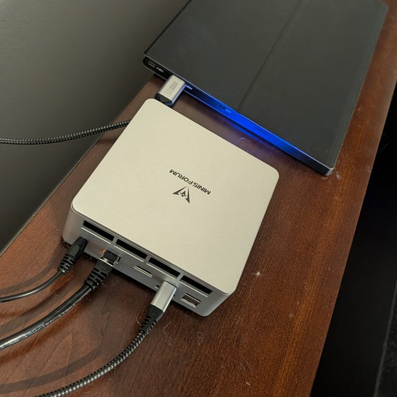 The Minisforum mini PC that runs the AI second brain, on a wooden desk with cables running out of the back